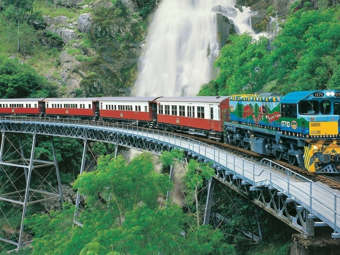 Kuranda Tour via Kuranda Scenic Rail and Skyrail – Small Group Tour Image 1 a train traveling down train tracks near a forest